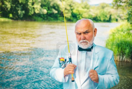 Photo for Portrait of senior businessman fishing. Excited mature man fisherman in white suit and bowtie with fishing rod, spinning reel on river - Royalty Free Image