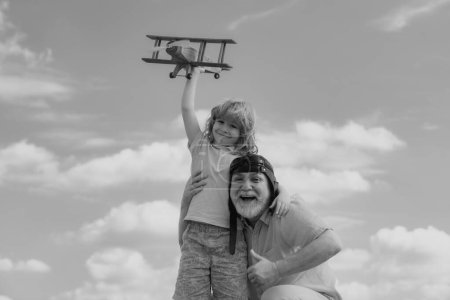 Photo for Old grandfather and young child grandson playing with plane together on blue sky. Cute boy with granddad playing outdoor - Royalty Free Image