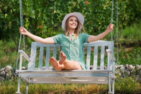 Téléchargez les photos : Portrait extérieur d'une jeune fille souriante et heureuse. Jeune femme sexy se balance sur une balançoire dans le jardin du parc d'été. Sensuelle fille blonde reposant dans le salon - en image libre de droit
