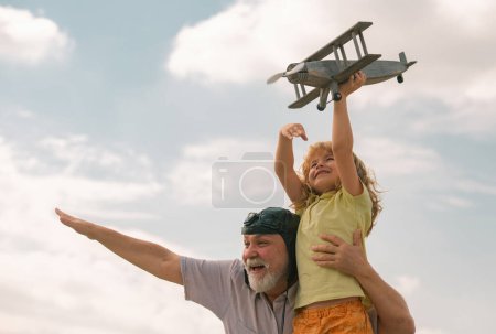 Téléchargez les photos : Enfant excité garçon et grand-père s'amuser avec avion en plein air sur fond de ciel avec espace de copie. Enfant rêve de voler, enfance heureuse avec grand-père - en image libre de droit