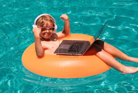 Foto de Negocios de verano. Feliz niño aprendiendo ordenador portátil en línea. Niño relajarse en el anillo flotante utilizando el ordenador en la piscina - Imagen libre de derechos