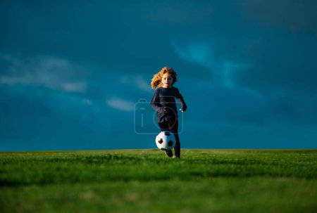 Téléchargez les photos : Un footballeur, un enfant joue au foot. Un gamin de foot jouant au foot. Enfant garçon jouer au football sur le terrain extérieur. Garçon coup de pied ballon de football - en image libre de droit
