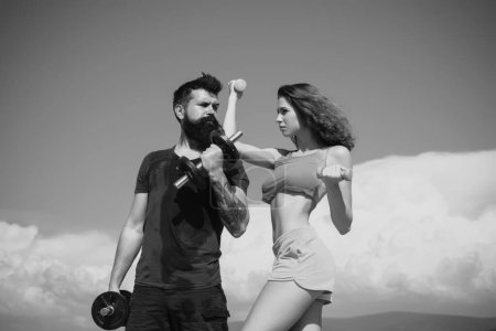 Photo for Fit couple doing exercising outdoors with dumbbell. Sportive woman and man, team. Sport, dumbbell and fitness, couple sports. Sporty sexy couple showing workout wiht dumbbells. Sports fitness girl - Royalty Free Image