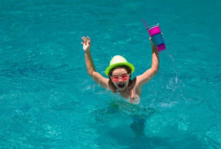 Téléchargez les photos : Un enfant qui boit du coctail dans la piscine. Petit garçon dans la piscine. Les enfants nagent en vacances d'été. Plage mer et l'eau amusant. Cocktail été enfants - en image libre de droit