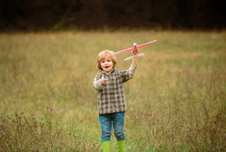 Photo for Kid having fun with toy airplane in field. Little boy with wooden plane, boy wants to become pilot and astronaut. Happy child play with toy airplane. Kids pilot dreams of flying on field - Royalty Free Image