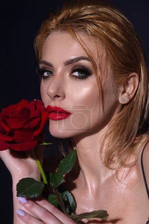 Téléchargez les photos : Maquillage lumineux. Portrait d'une jolie charmante fille rêveuse tenant des roses rouges, isolée sur fond de studio noir - en image libre de droit