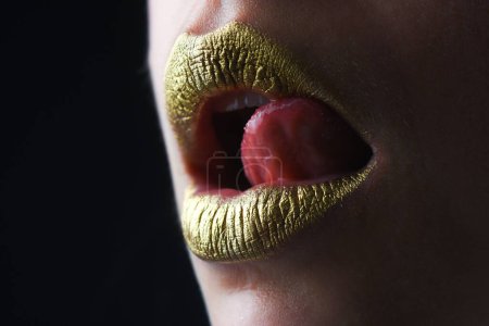 Photo for Sensual tongue licking lips. Golden glitter lipstick. Shine style for sexy lip. Sensual woman lips. Luxury golden mouth. Glamour gold lips. Golden lips with golden paint or metallic lipstick - Royalty Free Image