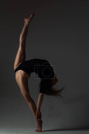 Leg-split. Sexy ballerina in black underwear stretching on black background. Concept of ballet art. Sexy pole dancer. Beautiful sexy fitness girl with great figure flexing her perfect body