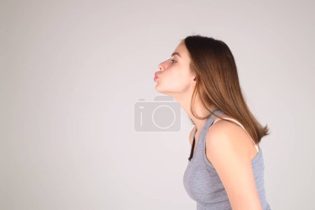 Photo for Portrait of lovely girl kissing you isolated on studio background. Pretty woman sends an air kiss. Pretty girl makes air kiss into camera, expresses her love. Affection and pleasant feelings - Royalty Free Image