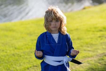 Photo for Kid boy practicing karate outdoor. Sport karate kids. Little boy wearing kimono doing karate in park. Little karate fighter. Martial arts for kids. Sport, action, combat sports - Royalty Free Image