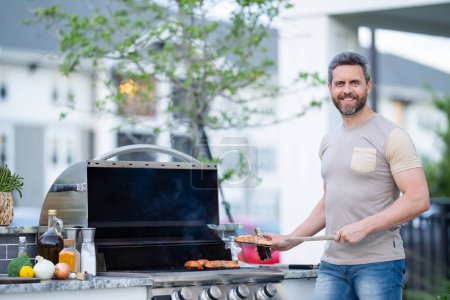 Photo for Hispanic man cooking on barbecue in the backyard. Chef preparing barbecue. Barbecue chef master. Man in apron preparing delicious grilled barbecue food, bbq meat. Grill and barbeque - Royalty Free Image