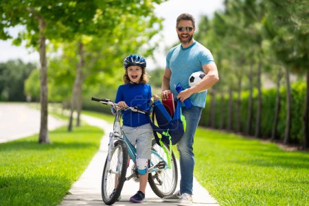 Photo for Father and son concept. Father helping son get ready for school. Father helping son to ride a bicycle. Little kid boy in safety helmet learning to ride cycle with his dad. Fathers day - Royalty Free Image