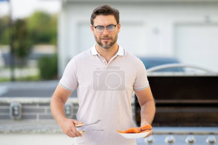 Photo for Grill chef cook. Guy with BBQ cooking tools. Barbecue and grill. Picnic and barbecue party. Chief cook with utensils for barbecue grill. Barbeque on holiday picnic. Man grilling a salmon fish on BBQ - Royalty Free Image