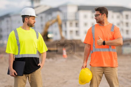 Photo for Two builders in a hard hat is busy working on a construction project at a site. A builders workes in a helmet near building construction sites - Royalty Free Image
