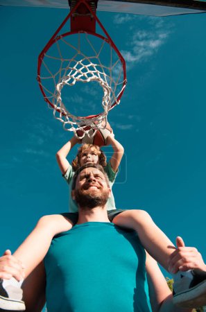 Foto de Padre e hijo jugando baloncesto. Padre cargando a su hijo en hombros en la cancha de baloncesto - Imagen libre de derechos