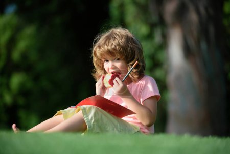 Téléchargez les photos : Mignon petit garçon étudier et manger de la pomme à l'extérieur - en image libre de droit