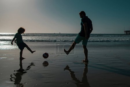 Photo for Daddy with kid boy on a summer day. Daddy with kid boy playing on a summer day. Father and son play soccer or football on the beach. Sporty family concept - Royalty Free Image