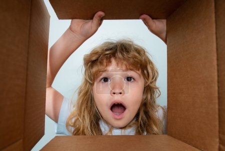 Photo for Excited child boy looking into the box, shipping cardboard box. Children expression surprised face - Royalty Free Image