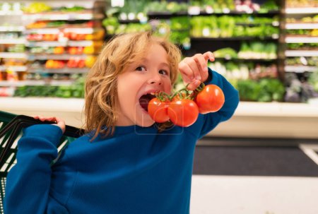 Téléchargez les photos : Enfant avec des tomates fraîches. Alimentation saine pour les enfants. Portrait d'un petit enfant souriant avec sac à provisions à l'épicerie ou au supermarché - en image libre de droit
