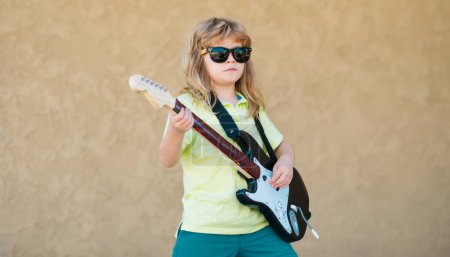Foto de Instrumentos musicales para niños. Divertido pequeño músico hipster niño tocando la guitarra - Imagen libre de derechos