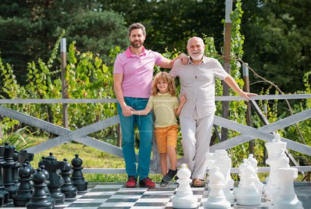Téléchargez les photos : Portrait de grand-père père père et fils jouant aux échecs. Des hommes heureux à différents âges jouant au jeu d'échiquier. Trois hommes génération - en image libre de droit