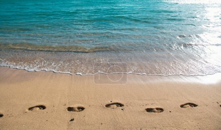 Fußabdrücke am Strand im Sandfußabdruck. Konzept für den Reise-Urlaub. Fußstapfen im Sand bei einem tropischen Sommerurlaub mit blauem Meer