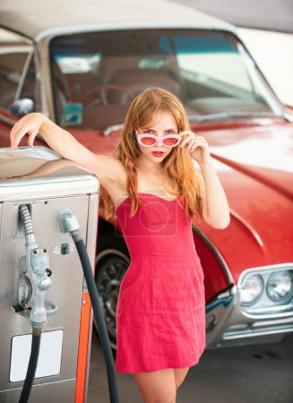 Foto de Sexy chica retro con coche. Gasolinera, mujer repostando el auto. Rojo automóvil retro - Imagen libre de derechos