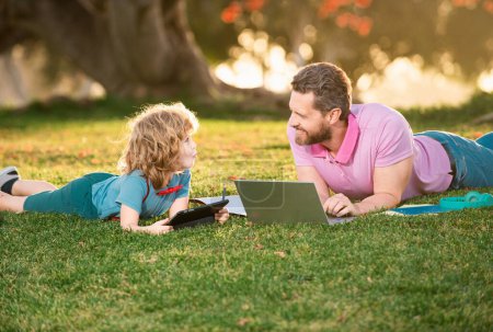 Foto de Hijo niño con padre aprendiendo al aire libre estudiando en línea y trabajando en el ordenador portátil - Imagen libre de derechos