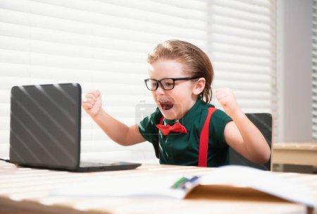 Téléchargez les photos : Enfant garçon utilisant un ordinateur portable et étudier leçon en ligne. Elève à l'école. Enfant mignon utilisant un ordinateur portable, étudier en ligne - en image libre de droit