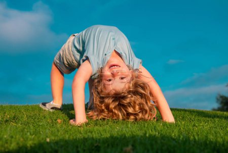 Téléchargez les photos : Happy kid girl debout à l'envers sur sa tête sur l'herbe dans la journée d'été - en image libre de droit