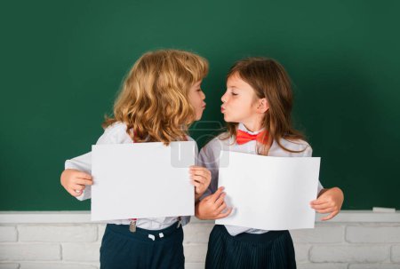 Photo for Kids love, first kiss. Back to school. Schoolchild friends back to school at knowledge day. Schoolkids holding white paper blank, poster with copy space - Royalty Free Image