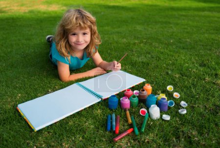 Téléchargez les photos : Enfants créatifs, développant l'imagination, la créativité. Un enfant dessine dans un parc d'été, peint de l'art. Petit artiste peintre dessiner des images en plein air - en image libre de droit