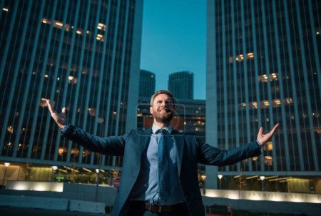 Téléchargez les photos : Un homme d'affaires se lève et passe la nuit en ville. Un homme d'affaires levant les bras près d'un immeuble de bureaux. Heureux, succès et triomphe des affaires, célébrant la victoire - en image libre de droit