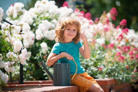 Téléchargez les photos : Mignon enfant arrose les plantes dans le jardin arrière-cour avec arrosoir. Pouce en l'air - en image libre de droit