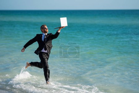 Photo for Freelance work, online business. Summer business. Businessman in suit hold laptop and run on sea. Funny businessman in a business suit with laptop standing in water. Remote business - Royalty Free Image