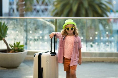 Téléchargez les photos : Les enfants voyagent. Voyageur enfant touristique en vêtements décontractés, lunettes de soleil de mode et chapeau tenir valise. Voyager à l'étranger week-ends. Voyage des enfants - en image libre de droit