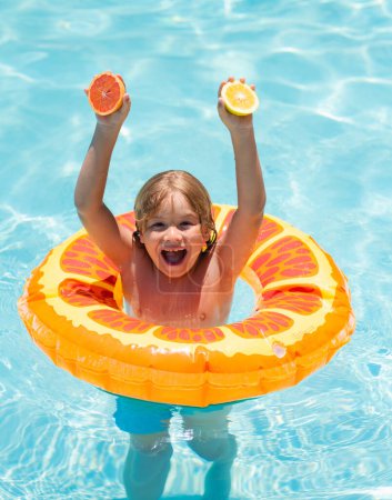 Foto de Niño flotando en una piscina en vacaciones de verano. Niño con naranja en la piscina. Frutas de verano. Niño feliz jugando con el anillo de natación en la piscina - Imagen libre de derechos