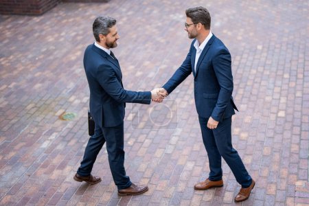 Photo for American business man shaking hands with partner, successful teamwork. Two business men shaking hands on street. Business men in suit shaking hands outdoors. Handshake between two business men - Royalty Free Image