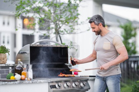 Photo for Handsome 40s man preparing barbecue. Male cook cooking meat on barbecue grill. Guy cooking meat on barbecue for summer family dinner at the backyard of the house - Royalty Free Image
