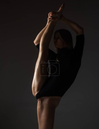 Fracture des jambes. Ballerine sexy en sous-vêtements noirs s'étirant sur fond noir. Concept d'art du ballet. Danseuse sexy. Belle fille de fitness sexy avec une grande figure fléchissant son corps parfait