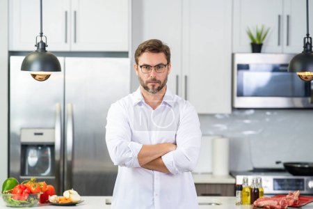 Photo for Man cooking food in kitchen. Handsome man cooking healthy food in kitchen. Guy cooking dinner food in kitchen. Home menu with fresh food ingredients. Modern kitchen interior - Royalty Free Image