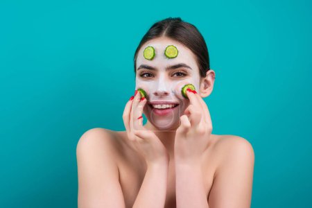 Téléchargez les photos : Facial mask of cucumber. Beautiful woman with facial mask with slices of fresh cucumber on face. Cosmetic masks on face. Portrait of beautiful spa girl. Beauty, healthcare - en image libre de droit