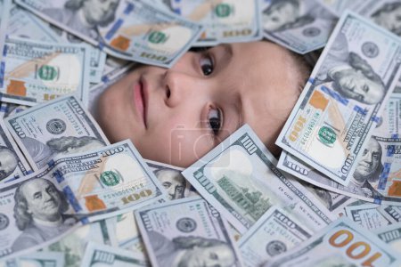 Foto de Los niños van en dinero. Cara de niño divertido en dólares dinero. Compras y concepto financiero - Imagen libre de derechos