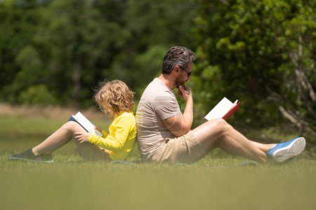 Photo for Outdoor school. Father and son reading book in park, man encourages boy to knowledge, family education. Father and child read bookin park. Parent reading with child book on summer nature in park - Royalty Free Image
