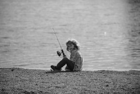 Téléchargez les photos : Le passe-temps des enfants. Pêche d'enfant sur le lac. Garçon avec fileuse à la rivière. Portrait de garçon excité pêche. Garçon à la jetée avec tige - en image libre de droit