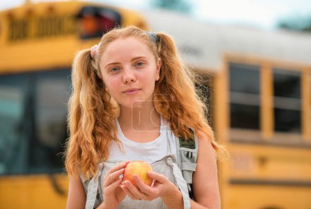 Téléchargez les photos : Écolière à l'avant de l'autobus scolaire avec pomme - en image libre de droit