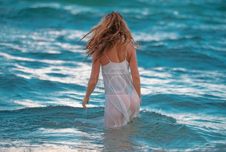 Téléchargez les photos : Jeune femme sexy en mer avec robe d'été transparente sexy. Plage d'été, corps de fille sensuelle. Fille en robe blanche sur les vacances à la plage tropicale - en image libre de droit