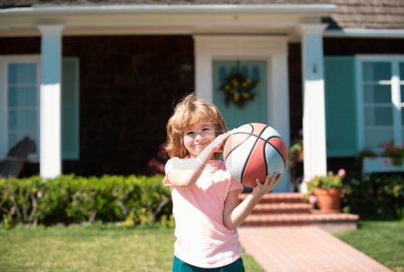 Téléchargez les photos : Un gamin qui joue au basket. Enfant posant avec une balle de basket à l'extérieur - en image libre de droit