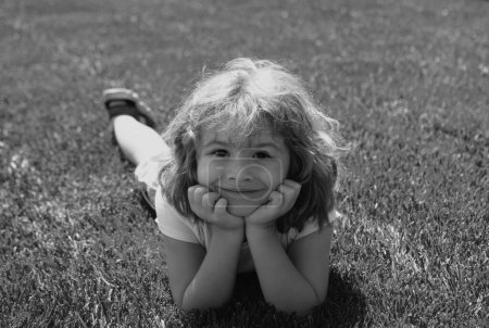 Foto de Primer plano retrato de un lindo niño tendido en la hierba en el parque natural de verano - Imagen libre de derechos