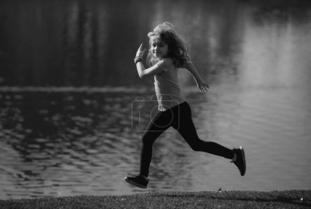 Photo for Kids running or jogging near lake on grass in park. Sporty child boy runner running in summer park. Active kids, sport children - Royalty Free Image